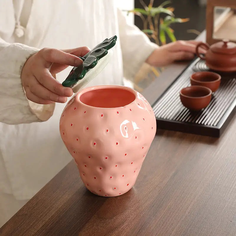 Pink strawberry-shaped ceramic tea canister with green leaf lid for strawberry tea storage