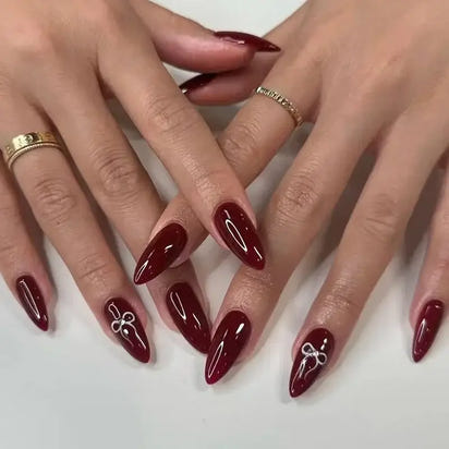 Burgundy stiletto nails with bow accents.