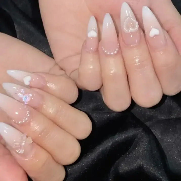Almond-shaped nails with heart and pearl embellishments.
