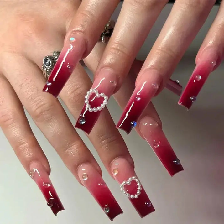Long, square, ombre red nails with pearl hearts and rhinestones.