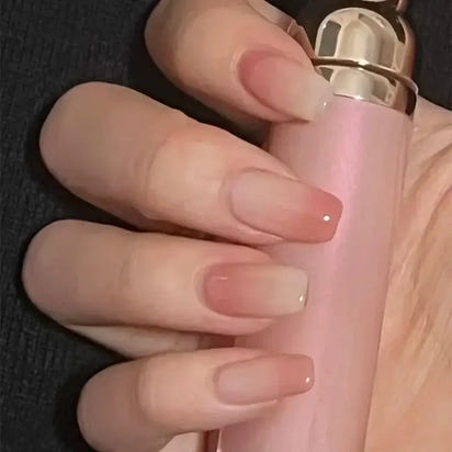 Hand holding pink lipstick with ombre nails.