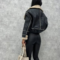 Person wearing a black leather jacket with beige trim against a gray wall