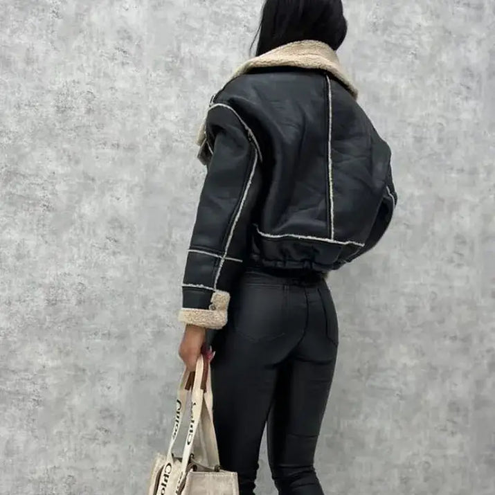 Person wearing a black leather jacket with beige trim against a gray wall