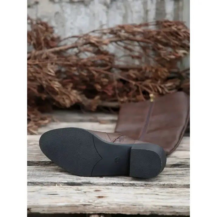Brown boot with black sole on a wooden surface with dried plants in the background