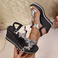 Black wedge sandals with butterfly embellishments.