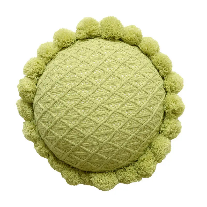Round, green, knitted pillow with pom-pom trim.