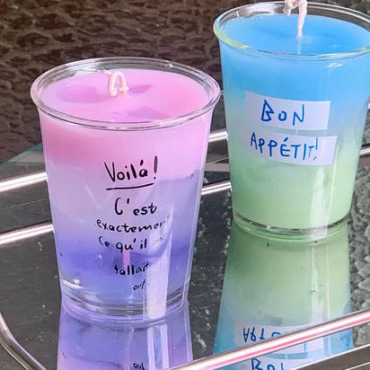 Two layered, colorful candles in clear glasses.