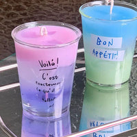 Two layered, colorful candles in clear glasses.