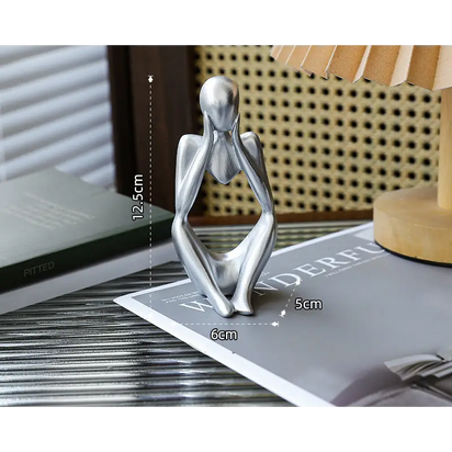 Silver-colored seated figure with hands on face.