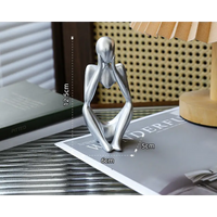 Silver-colored seated figure with hands on face.