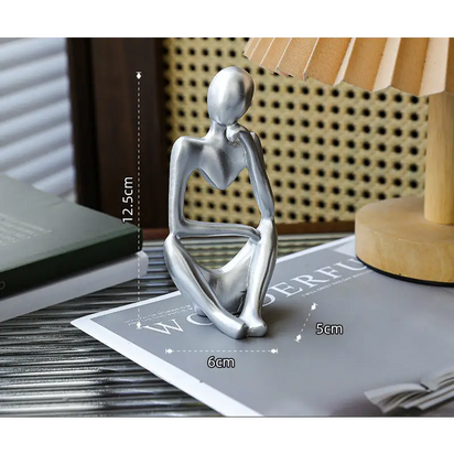 Silver-colored seated figure sculpture.