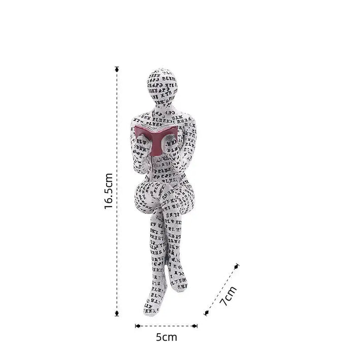 Figurine of a seated person covered in letters, reading a book.