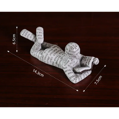 Figurine of a person reading a book, covered in text.