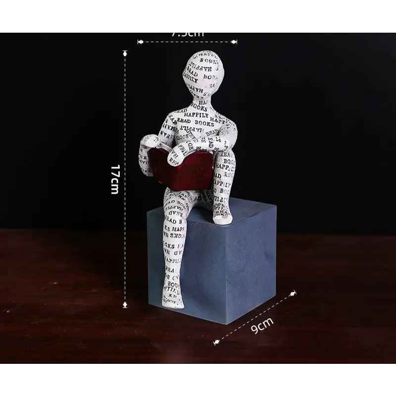 Figurine of a person reading a book, sitting on a cube.