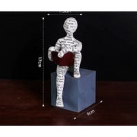Figurine of a person reading a book, sitting on a cube.