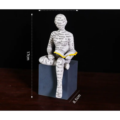 Figurine of a person reading a book, covered in words, sitting on a cube.