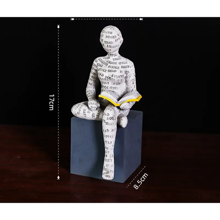 Figurine of a person reading a book, covered in words, sitting on a cube.