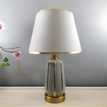 Gray and gold ceramic table lamp with white lampshade.
