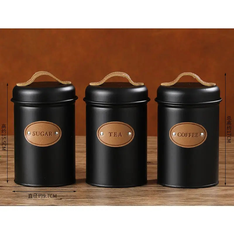 Three black wrought iron sealed canisters with leather handles and labels